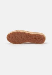 Shoe sole with a textured, brown rubber bottom and a woven, natural fiber edge. Features a curved shape for comfort and support.