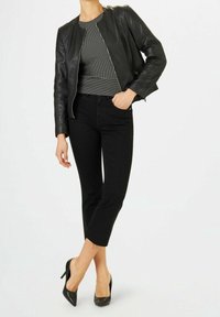 Veste en cuir noire portée sur un haut rayé noir et blanc, associée à un jean noir raccourci et des chaussures à talons noirs.