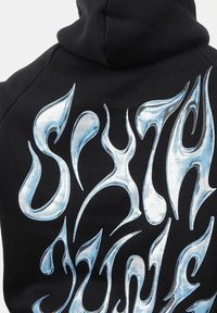 Sudadera negra con un gran gráfico de llamas azules brillantes en la parte de atrás, con curvas intrincadas y puntas afiladas, creando un aspecto dinámico.