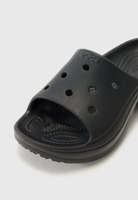 Sandale slide noire Crocs avec bout ouvert, trous de ventilation sur le dessus et semelle texturée pour le confort.