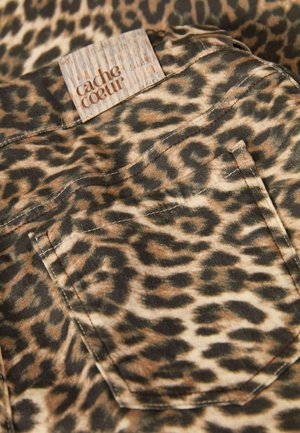 Leeuwenhuidprint stof met een kleine achterzak en een gestructureerd, lichtbruin label met "cache coeur" in reliëf, dat aardetinten en patronen toont.