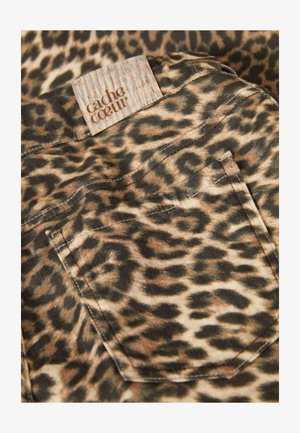 Leeuwenhuidprint stof met een kleine achterzak en een gestructureerd, lichtbruin label met "cache coeur" in reliëf, dat aardetinten en patronen toont.