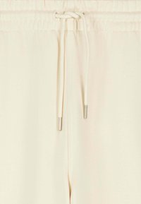 Close-up of beige elastic waistband pants with a tied drawstring featuring metal aglet tips in the center.