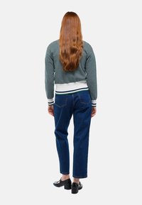 Pull en tricot vert et blanc avec un motif texturé, associé à un jean bleu taille haute et des chaussures à talons carrés noires. Vue de dos.