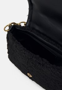 Sac à main noir texturé avec bandoulière chaîne dorée, rabat ouvert montrant l'intérieur en cuir lisse et fermeture à pression.