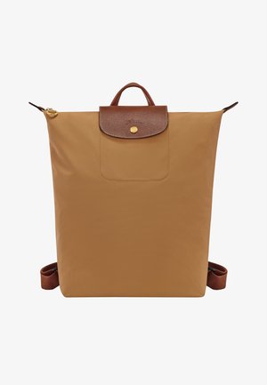 Tan nylon backpack featuring a brown leather flap with a gold button closure and an exterior pocket. Includes adjustable brown straps.