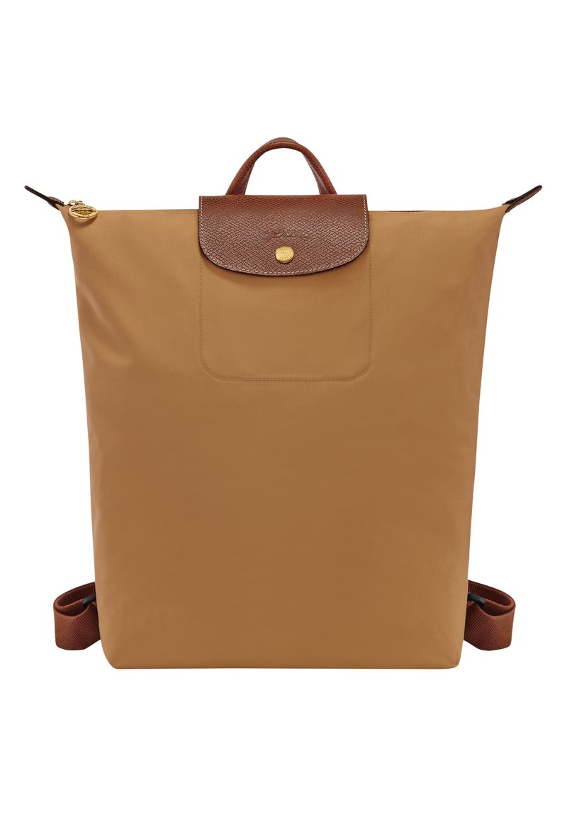 Tan nylon backpack featuring a brown leather flap with a gold button closure and an exterior pocket. Includes adjustable brown straps.