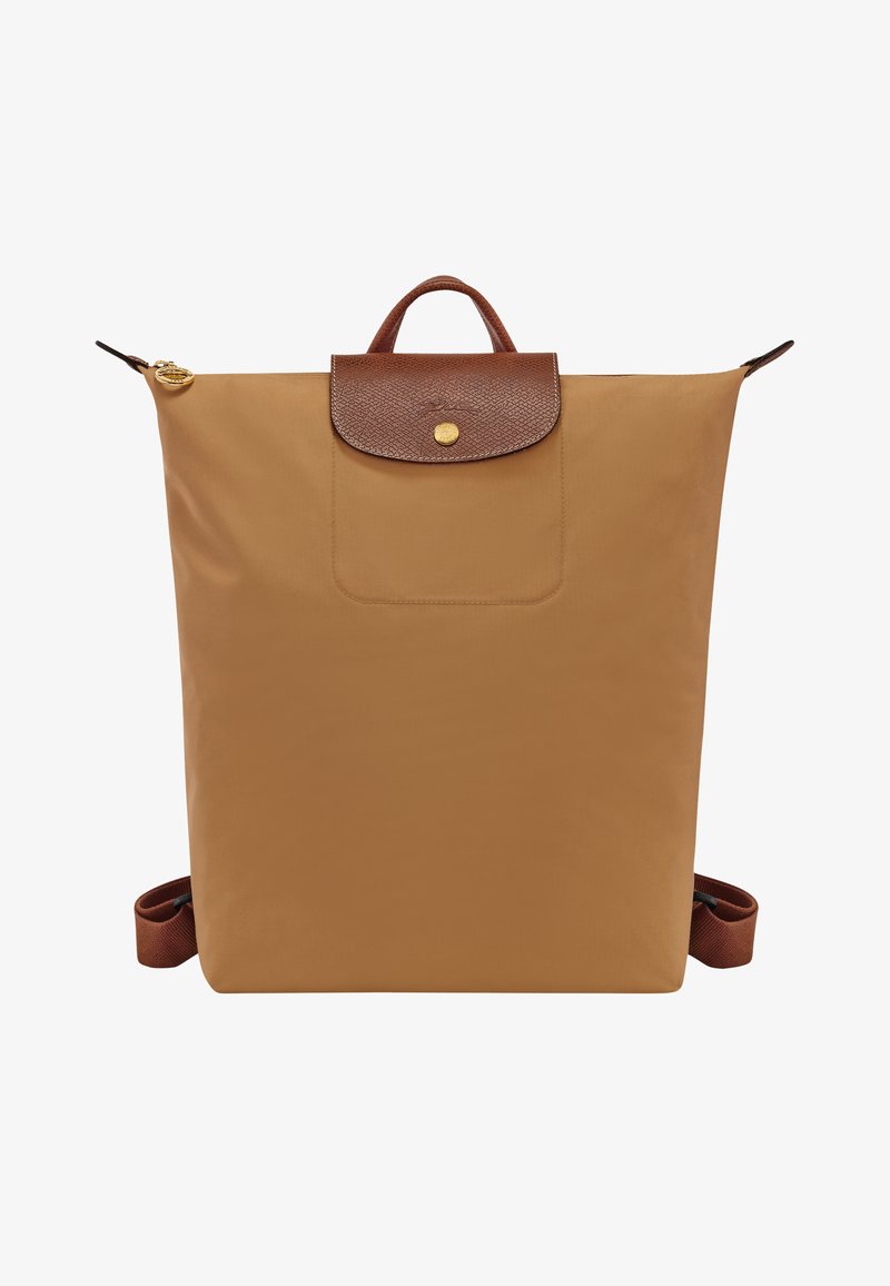 Tan nylon backpack featuring a brown leather flap with a gold button closure and an exterior pocket. Includes adjustable brown straps.