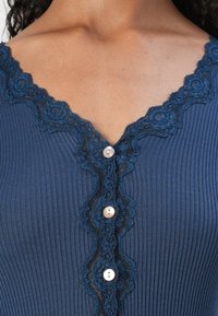 Haut côtelé navy avec un empiècement en dentelle festonnée le long de l'encolure, comportant trois boutons ronds en perles à l'avant pour la fermeture.