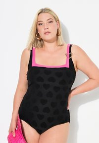 Zwarte badpak met hartpatroon, roze accenten op de vierkante halslijn en banden, en een hartvormige hardware detail op de linkerbasis.
