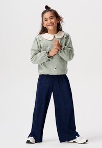 Lichtgroene sweatshirt met bloemborduring en een witte kraag, gecombineerd met marineblauwe ribbelachtige brede pijpen en witte sneakers.