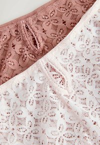 Gros plan sur un tissu en dentelle beige et blanc avec des motifs floraux et des bords festonnés, mettant en valeur une broderie détaillée et une texture riche.