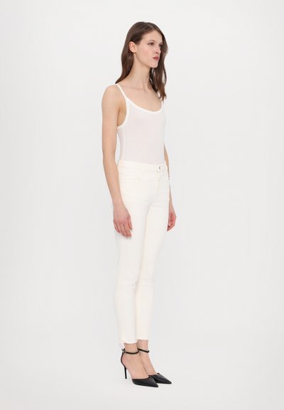 Baltā bezpiedurkņu blūze, pieguļošas baltas skinny džinsas un melni kurpi ar garu purngalu. Gluda auduma, eleganta griezuma, potītes siksniņa uz apaviem.