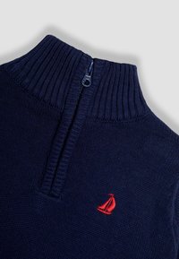 Pullover lavorato a maglia blu navy con colletto alto a costine e zip a un quarto, caratterizzato da un'emblema di un veliero rosso sul lato sinistro.