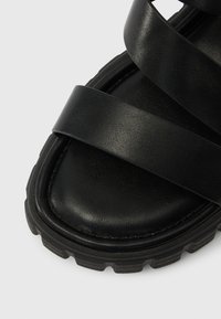 Μαύρη σανδάλι με λείο δερμάτινο επάνω μέρος και τρεις φαρδιές λουρίδες. Υφή στη σόλα για καλύτερη πρόσφυση και στρογγυλεμένο σχέδιο στα δάχτυλα.