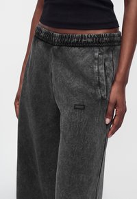 Άτομο που φοράει μαύρο cropped top με παντελόνι σκούρου γκρι με ελαστική μέση, πλαϊνές τσέπες και μικρό ορθογώνιο patch με το λογότυπο Hugo.