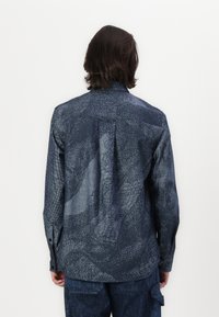 Camicia blu navy con bottoni realizzata in tessuto testurizzato, caratterizzata da un motivo astratto unico e un orlo dritto con polsini abbottonati.