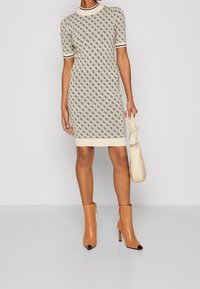 Robe tricotée à manches courtes en crème avec un motif en losanges ; dotée d'un col et de poignets contrastés. Associée à des bottes ankle beige et un sac à main léger.