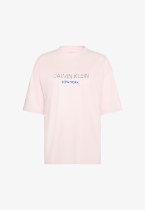 Lyserød bomulds-T-shirt, afslappet pasform, rund hals, korte ærmer. Indeholder "CALVIN KLEIN" og "NEW YORK" i blå med glitrende accenter.