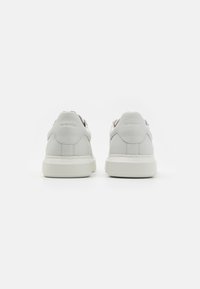 White leather sneakers with a textured finish, low profile, rubber sole, and minimal stitching. Features a neutral design with no visible logos.