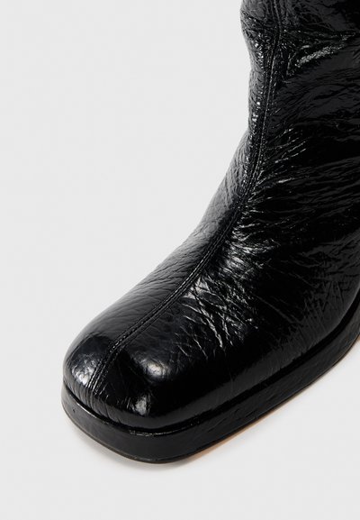 Botín negro de cuero hasta el tobillo con superficie texturizada, puntera redonda y detalle de costura lateral. Cuenta con un tacón bajo y grueso para mayor estabilidad.