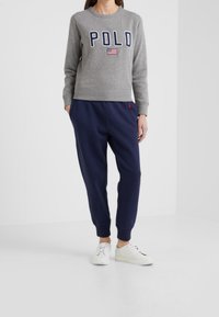 Grå sweatshirt med "POLO" text och en amerikansk flagga; i kombination med marinblå joggers och vita sneakers, som har ribbade muddar och midja.