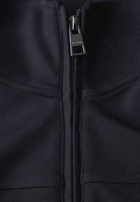 Laivaston sininen vetoketjullinen takki, jossa on sileä pinta, hopeinen vetoketju, rakenteelliset saumat, eikä näkyviä kuvioita tai logoja.