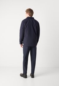 Chaqueta ligera en azul marino con un corte relajado, que presenta mangas largas, un cuello de botón y una tela texturizada, combinada con pantalones oscuros y botas.