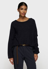 Maglione oversize di un blu navy scuro, con una texture morbida, scollatura ampia e cuciture delle spalle scese. Abbinato a pantaloni a vita alta e una cintura marrone.