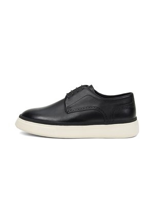 Chaussure derby en cuir noir avec lacets, semelle épaisse en caoutchouc blanc et détails subtils de brogue sur le côté et le talon.