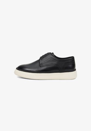 Chaussure derby en cuir noir avec lacets, semelle épaisse en caoutchouc blanc et détails subtils de brogue sur le côté et le talon.