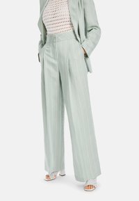 Hellgrüne gestreifte Hose aus einem weichen Stoff, mit hoher Taille, weitem Bein und seitlichen Taschen. Getragen mit weißen Open-Toed-Absätzen.