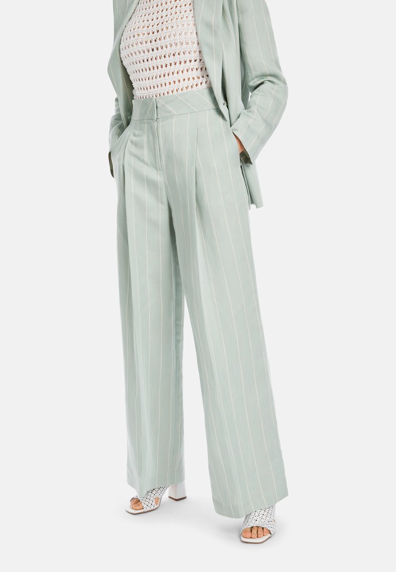 Hellgrüne gestreifte Hose aus einem weichen Stoff, mit hoher Taille, weitem Bein und seitlichen Taschen. Getragen mit weißen Open-Toed-Absätzen.
