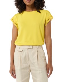 Yellow top with short sleeves, featuring lace trim at the shoulders. Paired with light beige high-waisted trousers, made of a smooth fabric.