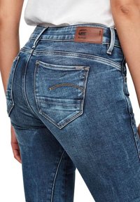 Jeans de mezclilla azul desteñidos con una cintura alta, que presentan un parche de cuero marrón, dos bolsillos traseros y una tela texturizada.