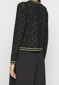 Czarna kurtka z teksturowanym wzorem oraz kontrastującym neonowo żółtym kołnierzem i brzegiem. Długie rękawy o luźnym kroju.