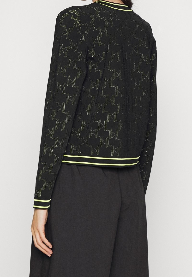 Czarna kurtka z teksturowanym wzorem oraz kontrastującym neonowo żółtym kołnierzem i brzegiem. Długie rękawy o luźnym kroju.
