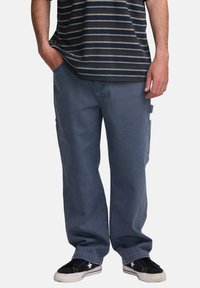 Sötét szürke denim cargo nadrág, laza szabással, oldalsó zsebekkel és sima textúrával, párosítva egy tengerészkék csíkos pólóval és fekete sportcipővel.