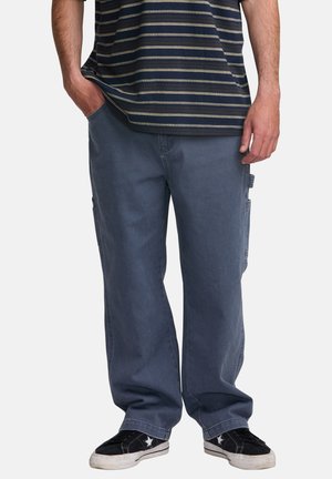Cargo pants in dark grey denim with a loose fit, side pockets, and a smooth texture, paired with a navy-striped T-shirt and black sneakers.