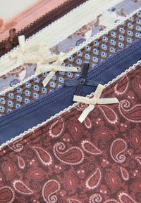 Pile de sous-vêtements pour femmes à motifs en paisley marron, bleu marine, géométrique bleu, floral blanc, marron foncé et nuances de rose avec petits nœuds en tissu.