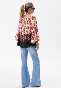Blumenbluse mit Glockenärmeln in Pink und Grün, mit einem gerafften Ausschnitt. Kombiniert mit hellblauen Schlagjeans.