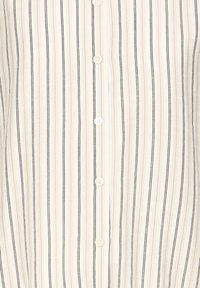 Tuvaudums balta auduma ar vertikālām bēšām un melnām svītrām un baltām pogām, kas izšūtas vertikālā līnijā.