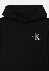 Felpa nera con cappuccio, caratterizzata da una texture morbida, un cappuccio con coulisse e un logo bianco di Calvin Klein sul lato sinistro del petto. Design semplice e senza motivi.