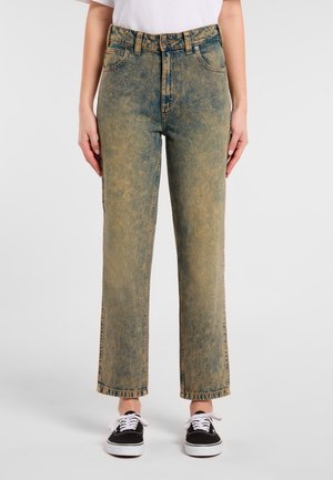 Jeans de mezclilla de talle alto en azul desteñido con corte recto, que presentan costuras visibles y un ligero efecto de desgaste. Combinados con zapatillas negras.