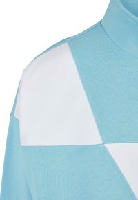 Ljusblå polo med vita vinklade färgblock. Mjuk, strukturerad tyg med en formad krage och noggrant sydda detaljer.