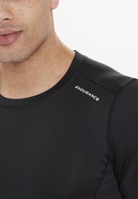 Schwarzes Sportshirt mit Rundhalsausschnitt und nahtlosem Design, mit dem Wort "ENDURANCE" in Weiß auf der Schulter bedruckt.