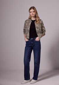 Veste bomber à imprimé léopard sur un top noir, associée à un jean droit bleu et des sneakers blanches, avec une texture de tissu lisse.