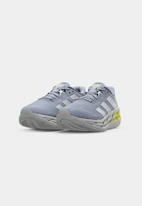Baskets de sport grises avec une tige en mesh, des rayures blanches et une semelle en caoutchouc texturée avec des accents jaune fluo pour une meilleure visibilité.