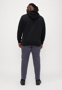 Black hooded sweatshirt with a relaxed fit, paired with gray pants. The fabric is smooth, and the design features ribbed cuffs and hem.