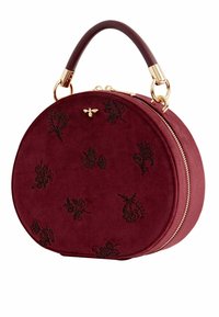 Ronde burgundy suède handtas met gouden hardware, bovenhandvat en gegraveerde bloempatronen. Bevat een ritssluiting en een decoratieve bijdetails.